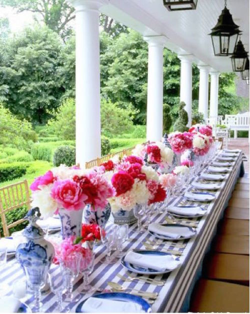 A Carolyne Roehm tablescape featuring pink and red garden roses in blue and white porcelain vases on a striped tablecloth.