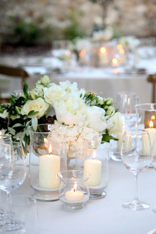A white wedding centerpiece with hydrangeas, roses, and candles in glass hurricanes.