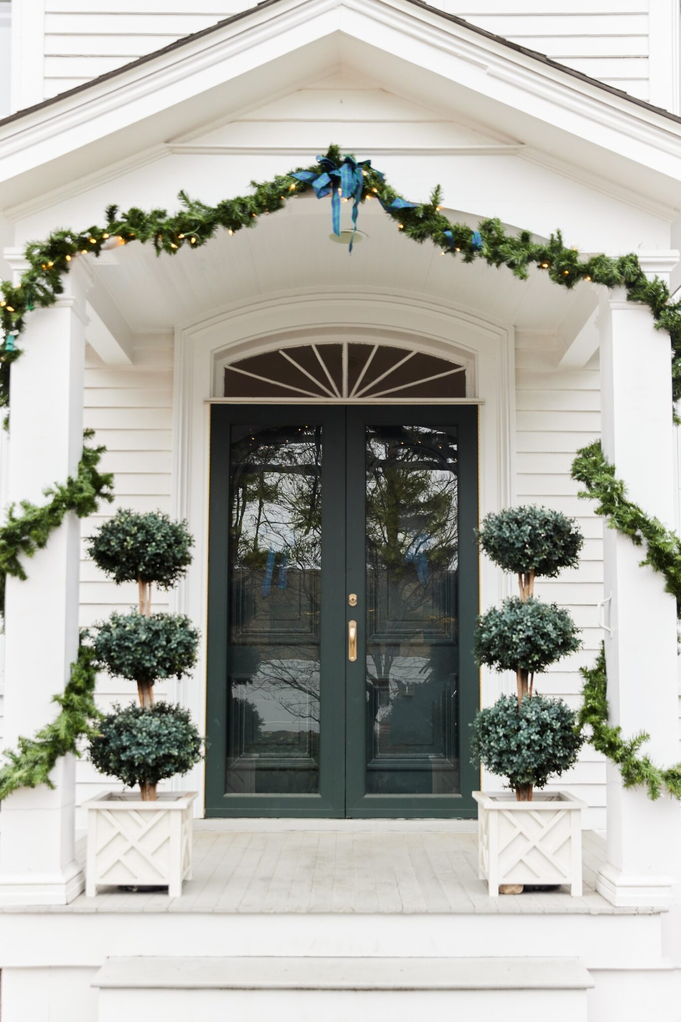 front-porch-with-garland-around-columns-and-faux-boxwood-topiaries-in-chippendale-planters